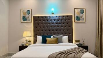 Ein Hotelzimmer mit einem großen Bett, einem gepolsterten Kopfteil, zwei Nachttischen mit Lampen und Kunstwerken an den Wänden.