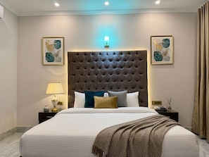 A hotel room with a large bed, a tufted headboard, two bedside tables with lamps, and artwork on the walls.