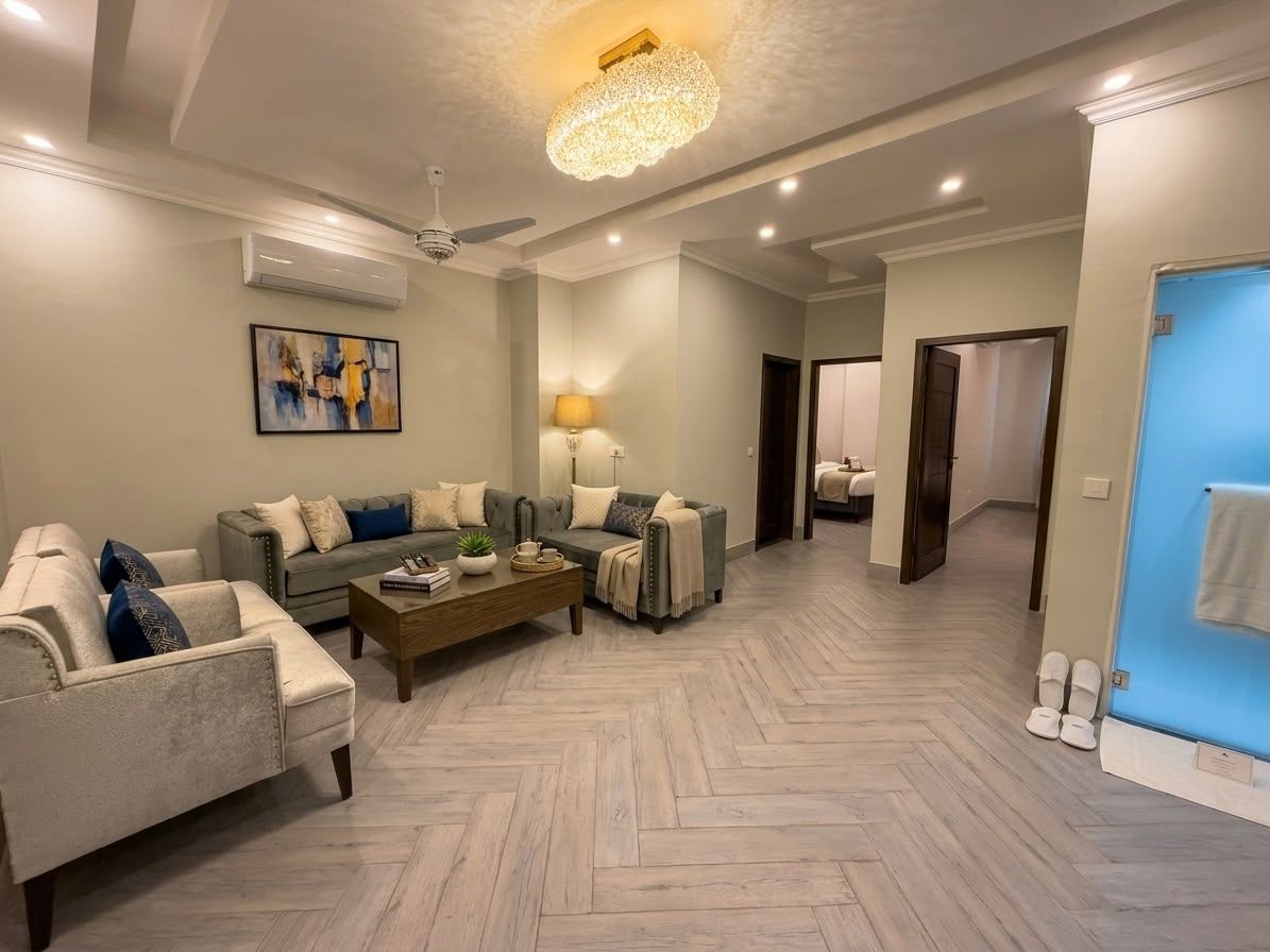 Un salon moderne avec un parquet en chevrons, un ensemble de canapés, une table basse et un lustre.