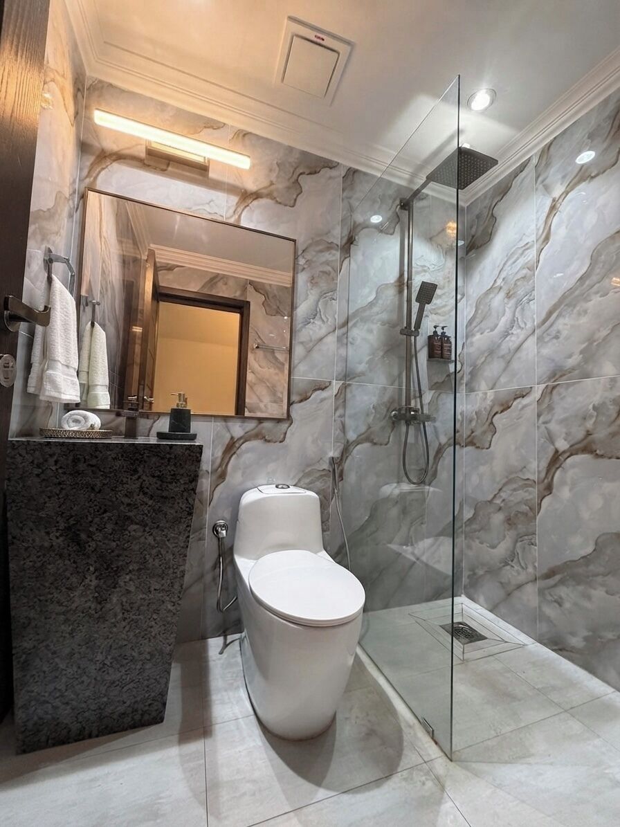 A modern bathroom with a marble wall, a glass shower enclosure, a white toilet, and a granite countertop.