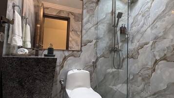 A modern bathroom with a marble wall, a glass shower enclosure, a white toilet, and a granite countertop.