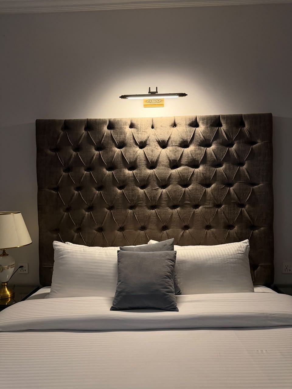 Ein Hotelzimmer mit einer gepolsterten Kopfteile, einer Nachttischlampe und einem Bett mit Kissen.