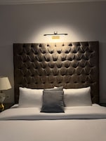 Una habitación de hotel con cabecera capitonada, una lámpara de noche y una cama con almohadas.