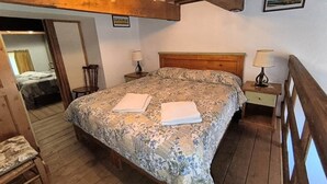 A bedroom with a wooden bed, two bedside tables, a wooden chair, and a wooden ceiling. - Chalet in Maremma with Private Pool and Wi-Fi, Apt 23 (Castel del Piano)