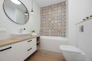A modern bathroom with a round mirror, white sink, and a bathtub. - Unique Apartment for 6 People | Balcony & Parking (Warszawa)
