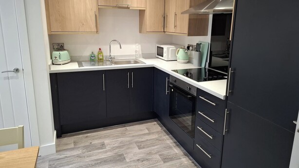 A modern kitchen with wooden cabinets, a stainless steel range hood, a microwave, and a kettle. - Sleeps2-centrallocation-familyfriendly-newrefurb (Retford)