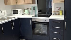 A modern kitchen with wooden cabinets, a microwave, a kettle, and a built-in oven. - Sleeps2-centrallocation-familyfriendly-newrefurb (Retford)