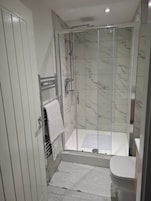 Un baño moderno con ducha acristalada, inodoro blanco y barra para toallas.