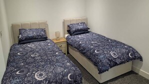 A bedroom with two beds, each with a headboard and a bedside table with a lamp. - Sleeps2-centrallocation-familyfriendly-newrefurb (Retford)