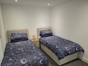 Un dormitorio con dos camas, cada una con cabecera y mesita de noche con lámpara.