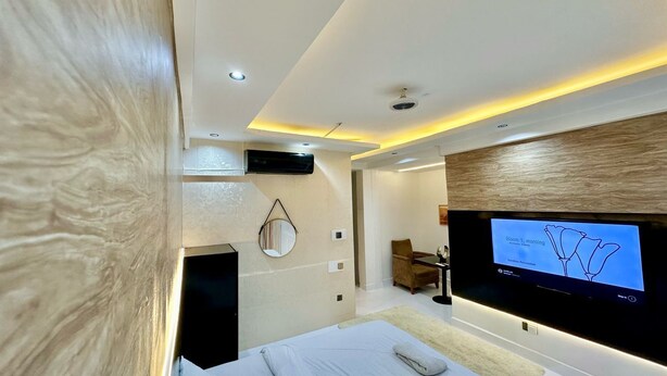 A modern hotel room with a bed, a TV mounted on the wall, a desk, and a chair. - Blevama Homes (Dar es Salaam)