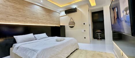 A modern bedroom with a large bed, recessed lighting, a wall-mounted air conditioner, and a TV on the wall.