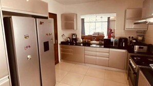 A modern kitchen with stainless steel appliances, a central island, and a view to the dining area. - Blevama Homes (Dar es Salaam)