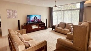A living room with a TV, sofas, and a large window. - Blevama Homes (Dar es Salaam)