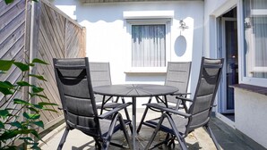 En uteplats med ett runt bord och fyra stolar, ett trästaket och ett fönster med en gardin.