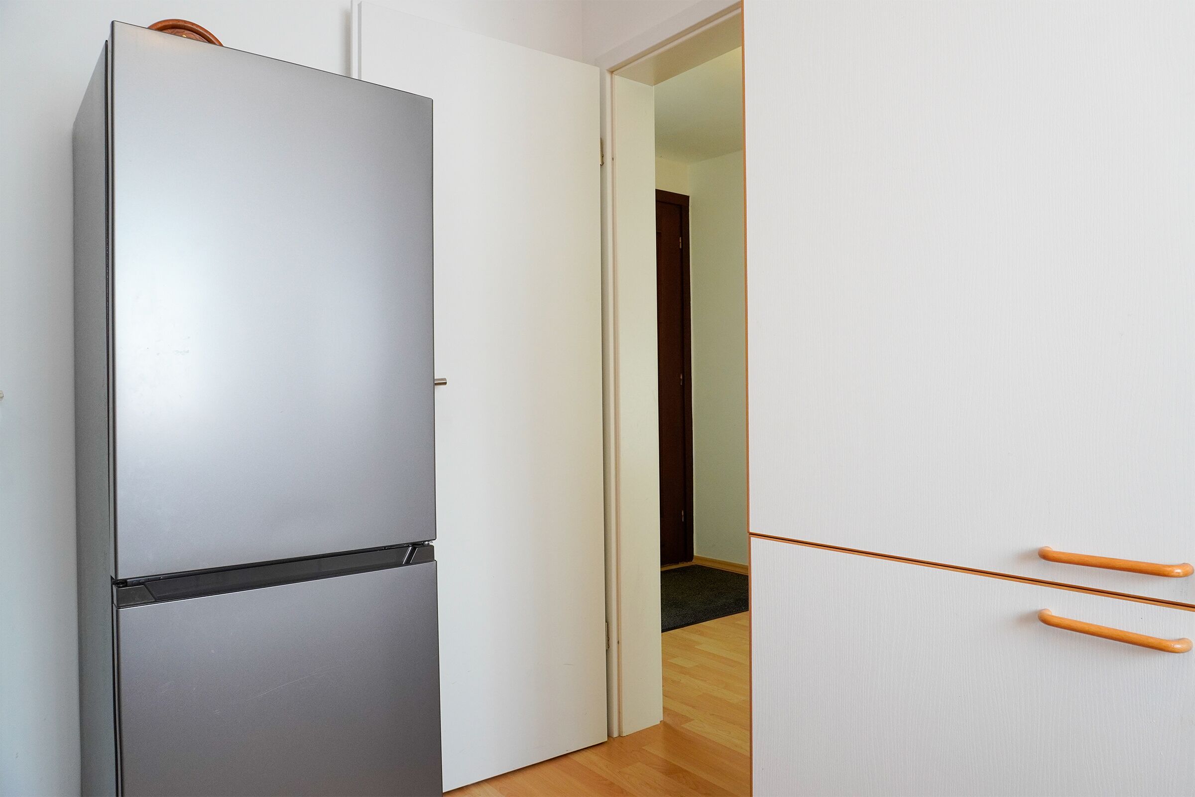 Une cuisine moderne avec un réfrigérateur en acier inoxydable, un meuble blanc doté de poignées en bois et un plancher en bois.