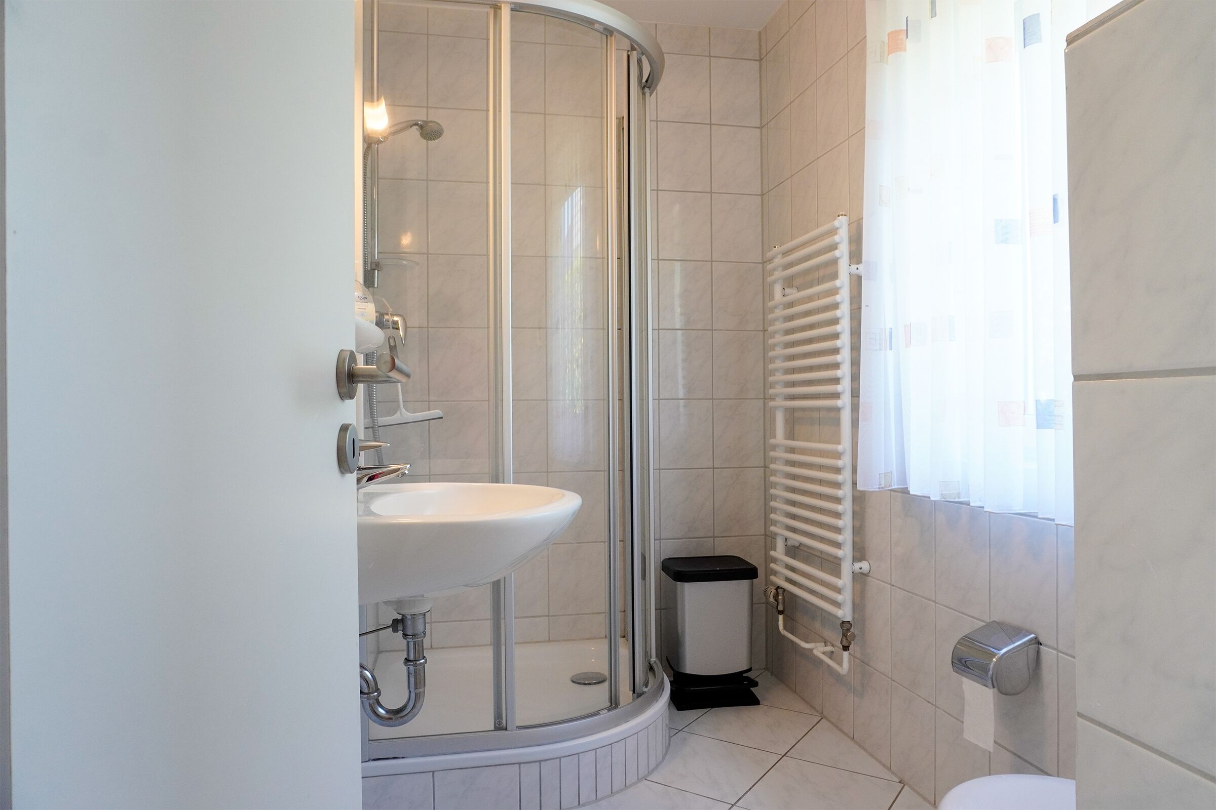 Ein Badezimmer mit Dusche, Waschbecken, Toilette und einem fenster mit Vorhängen.