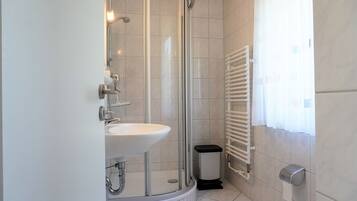Ein Badezimmer mit Dusche, Waschbecken, Toilette und einem fenster mit Vorhängen.