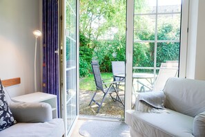 A room with a sofa, a chair, a small table, and a view through a glass door to an outdoor area with a table and chairs. - Lotte Vacation Rental for up to 4 People (Non-Smoking) (Niendorf/ostsee)