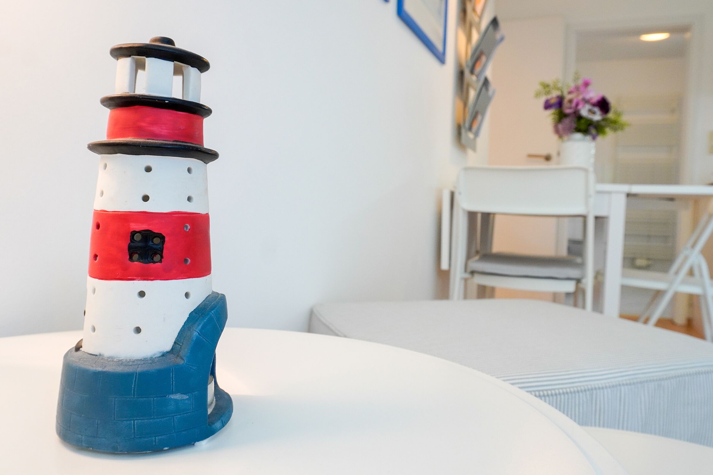 A model lighthouse on a white table in a room with a white chair and a white door in the background.