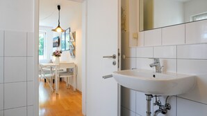 Ein modernes Badezimmer mit einem weißen Waschbecken, einem Spiegel und einer Tür zu einem Essbereich mit Tisch und Stühlen.