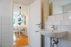 A modern bathroom with a white sink, a mirror, and a door leading to a dining area with a table and chairs. - Lotte Vacation Rental for up to 4 People (Non-Smoking) (Niendorf/ostsee)