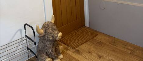 A wooden door with a 'Welcome' sign above it, a small rug, and a metal rack with a horned animal figure.