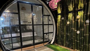 A modern, circular room with glass walls, a bed, and a small seating area.