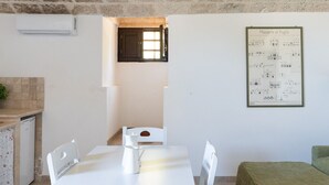 Un comedor con una mesa blanca, sillas, un ventanal pequeño y un cartel arquitectónico enmarcado en la pared.