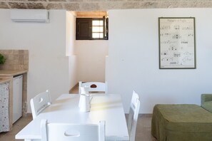 Ein Essbereich mit einem weißen Tisch, Stühlen, einem kleinen Fenster und einem gerahmten Architekturplakat an der Wand.
