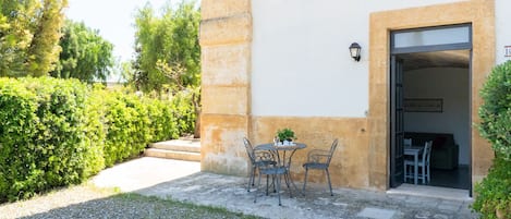 Un patio con una mesa, sillas, una puerta que da a una habitación y un muro de piedra.