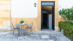 Un espacio al aire libre con mesa y sillas, una planta en maceta y una puerta que da a un espacio interior.