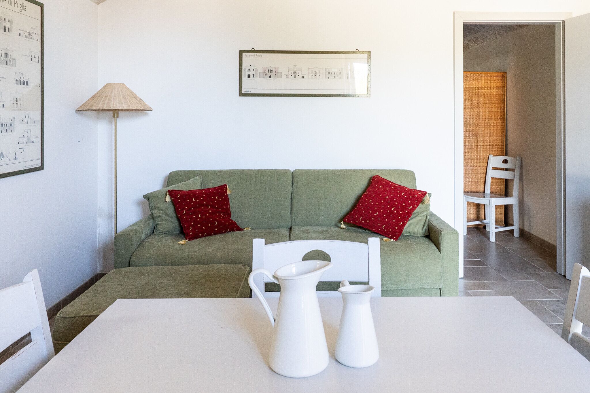 A living room with a green sofa, two red pillows, a white table, and a white chair.