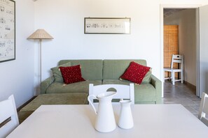 Ein Wohnzimmer mit einem grünen Sofa, zwei roten Kissen, einem weißen Tisch und einem weißen Stuhl.