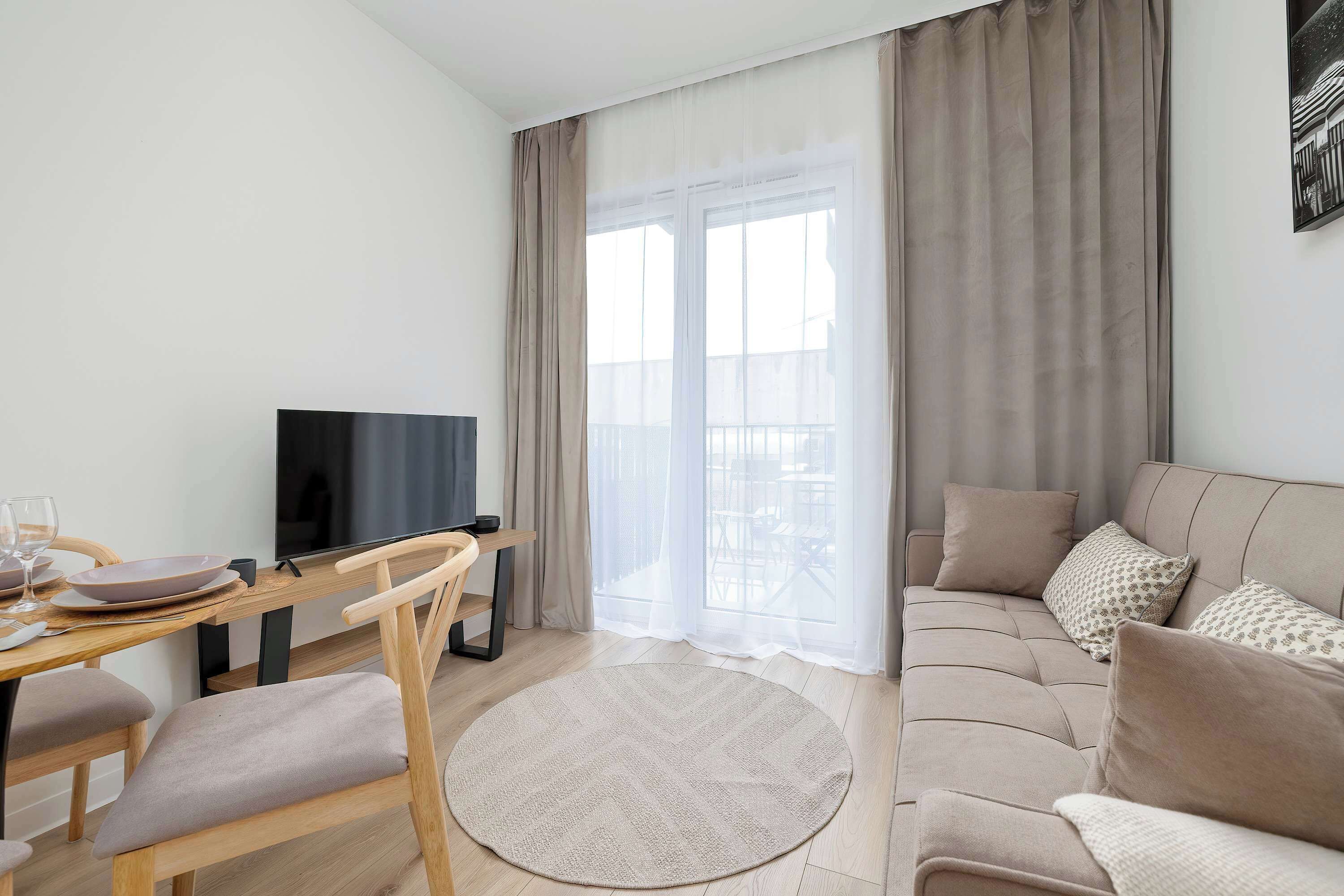 Bright living room with a comfortable sofa, TV, dining table, and large windows overlooking the balcony.
