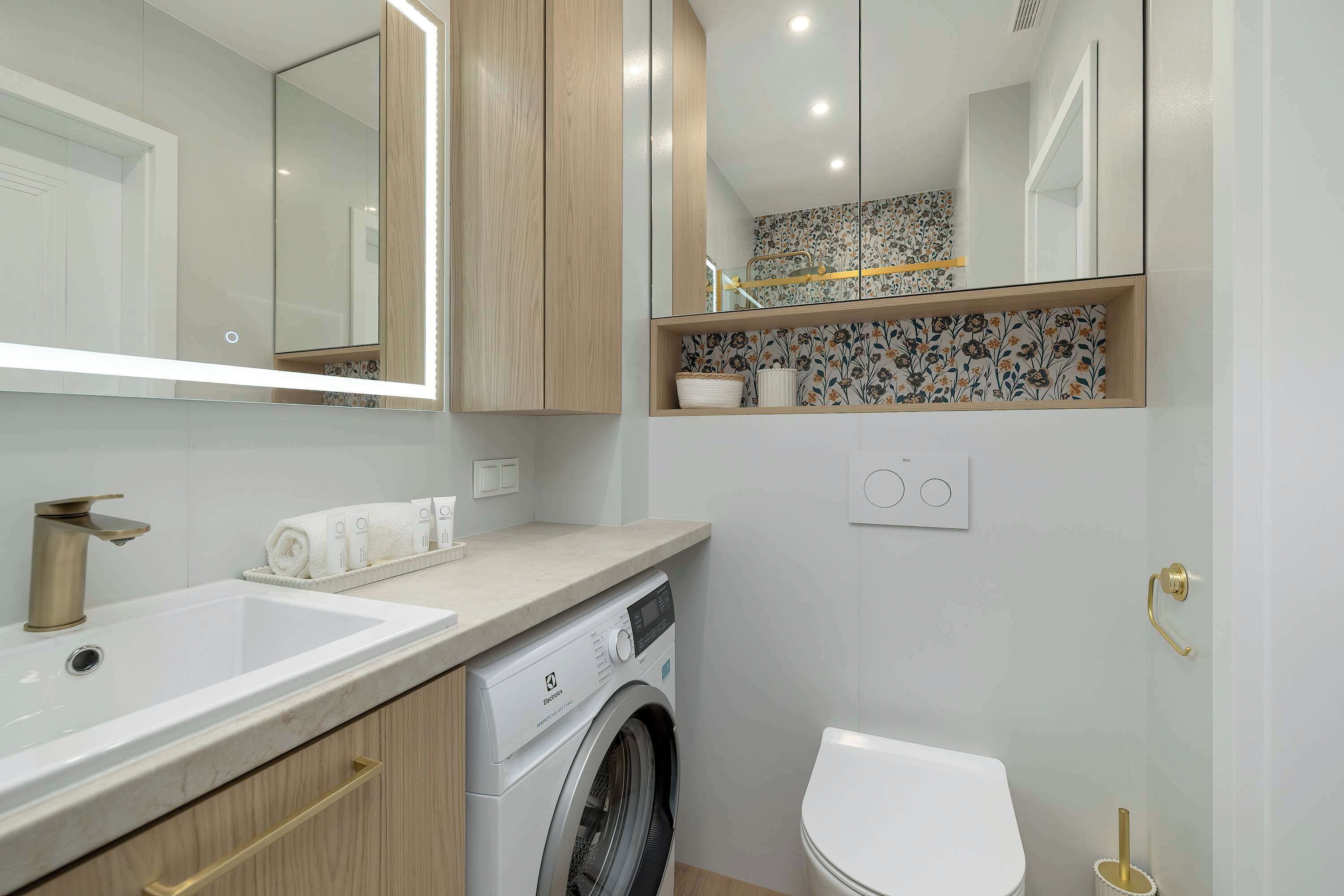 Ein modernes Badezimmer mit Waschbecken, Waschmaschine, Toilette und einem Spiegel mit integrierter Beleuchtung.