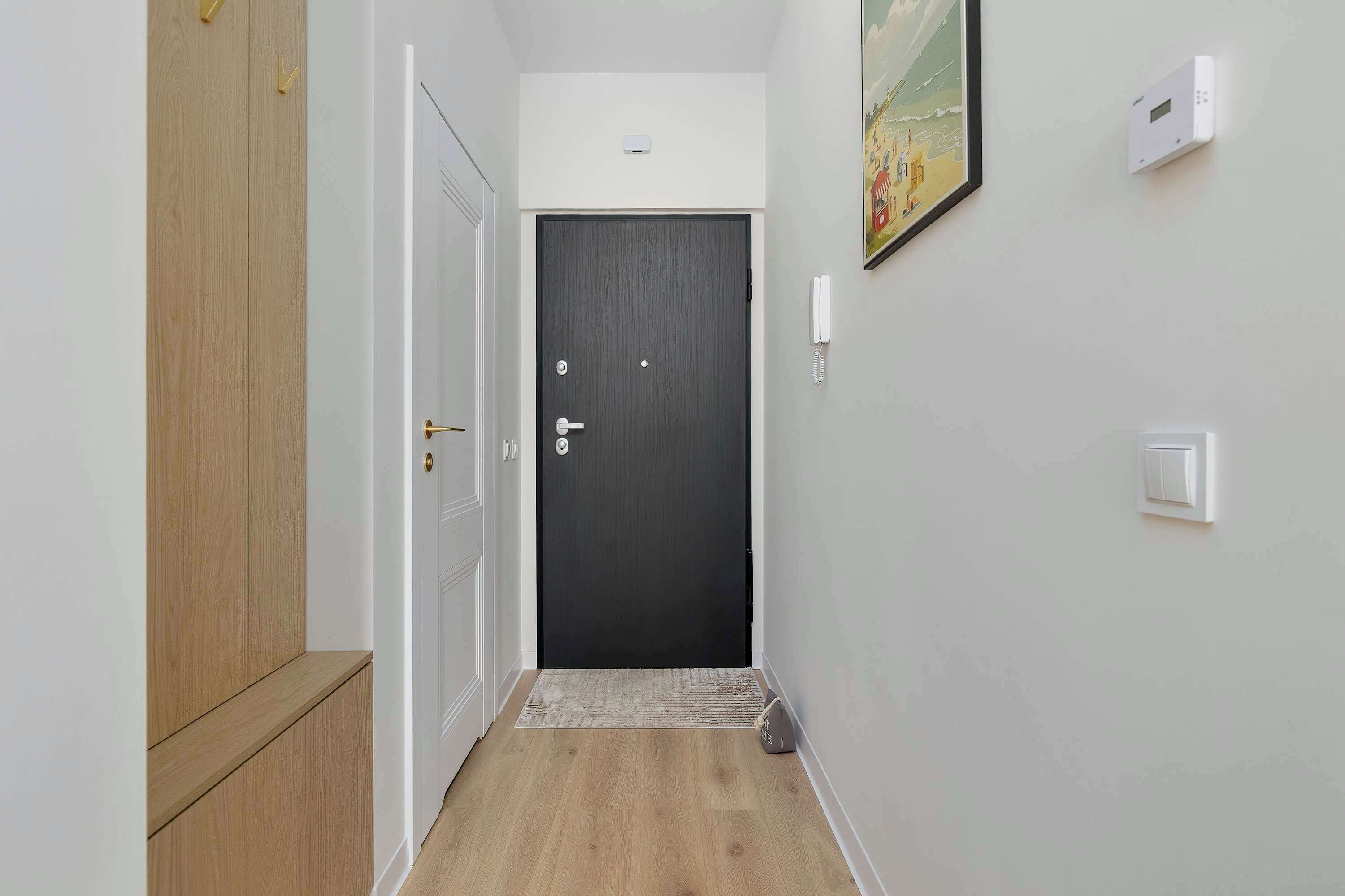 A hallway with a dark door, a white wall with a phone, and a painting.