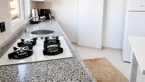 Una cocina con encimera de granito, cuatro hornillas, un fregadero y un refrigerador blanco.