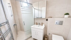 Un baño moderno con cabina de ducha de vidrio, un lavabo blanco y un inodoro.