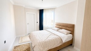 Un dormitorio con cama, una puerta, una ventana con cortinas y una lámpara en el techo.