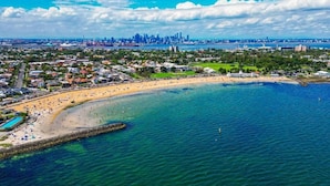 An aerial view of a coastal city with a prominent beach, a marina, and a skyline with high-rise buildings. - Stylish Williamstown 3BR | Beach, CBD & Museum (Williamstown North)