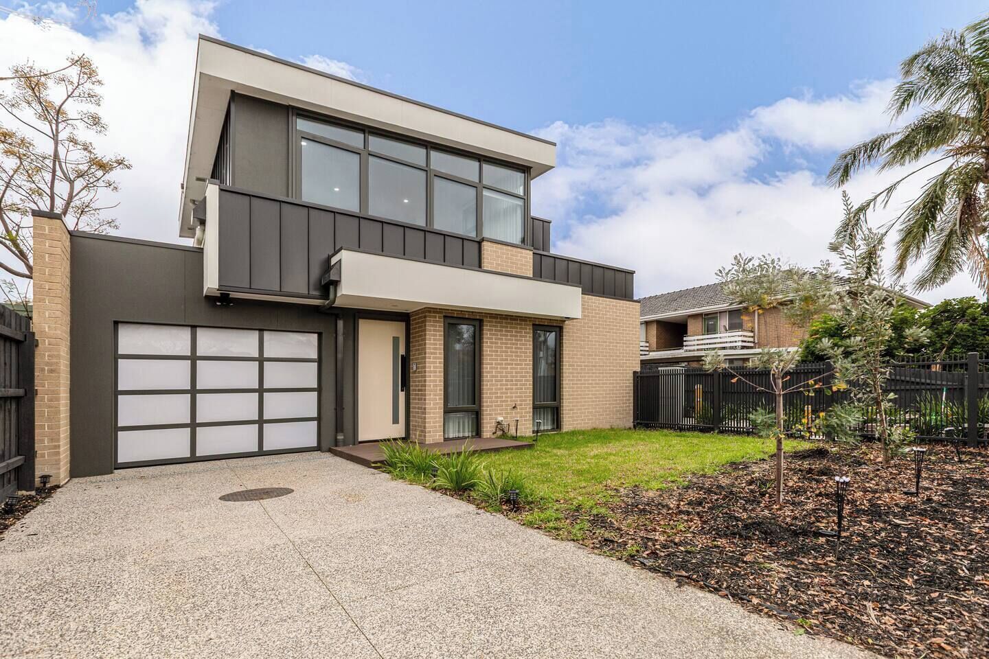 A modern two-story house with a garage, a small front yard, and a fence.