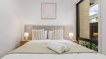 A hotel room with a large bed, two bedside tables with lamps, a framed picture on the wall, and a window with a view of greenery.