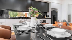 A modern kitchen with dark cabinets, a dining table set for four, and a view of the outdoors. - Stylish Williamstown 3BR | Beach, CBD & Museum (Williamstown North)
