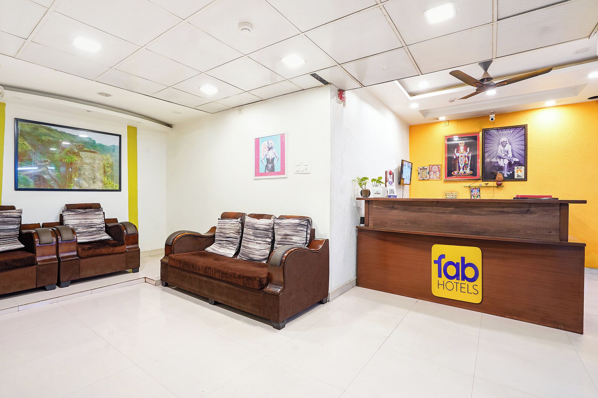 A hotel reception area with a reception desk, a brown sofa with striped cushions, and a large framed landscape painting on the wall.