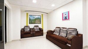 Un área de espera con un sofá marrón, dos sillones y un cuadro de paisaje en la pared.