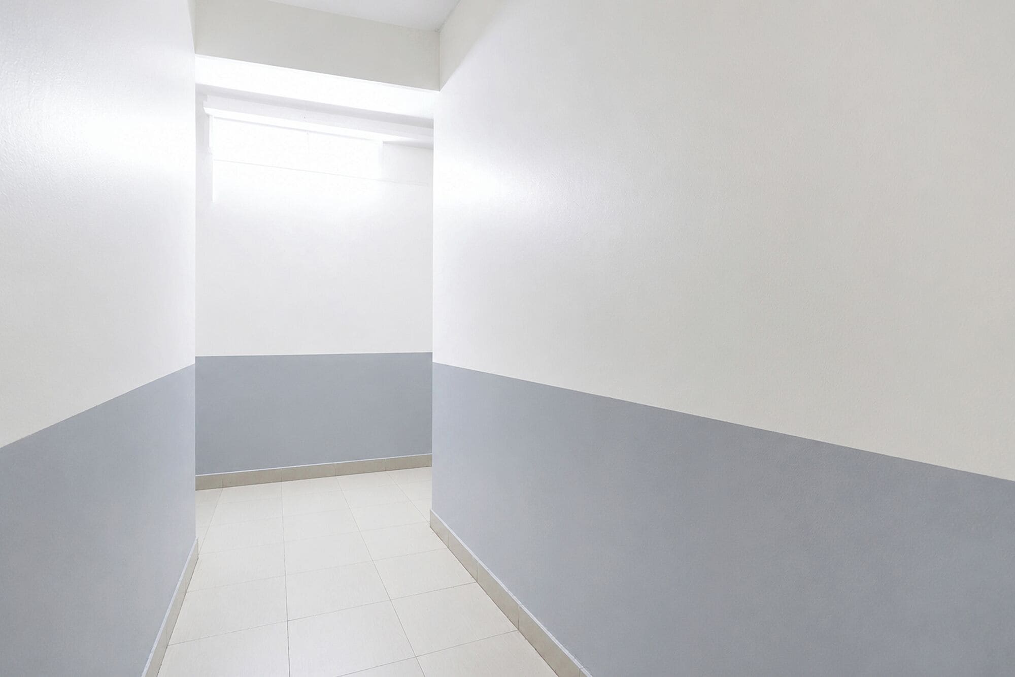 A narrow hallway with white and grey walls, a tiled floor, and a ceiling light.
