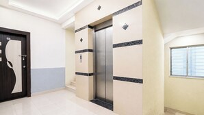 Un pasillo con una puerta marcada '101', un ascensor mural y un ventanal con persianas.