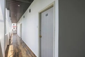Un pasillo largo y estrecho con piso de madera, paredes blancas y una puerta cerrada con placa numérica.