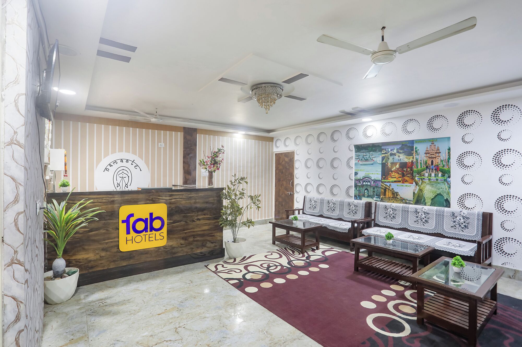 A hotel reception area with a reception desk, seating, ceiling fans, and decorative wall art.